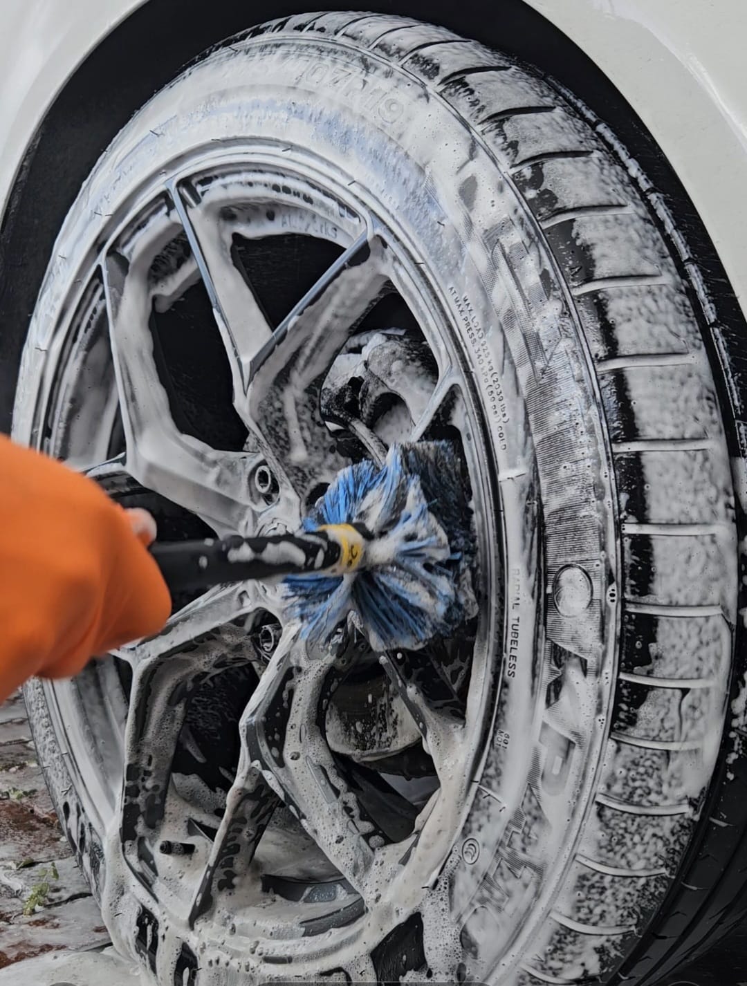 Wheel and tyre covered in foam being cleaned with a soft detailing brush
