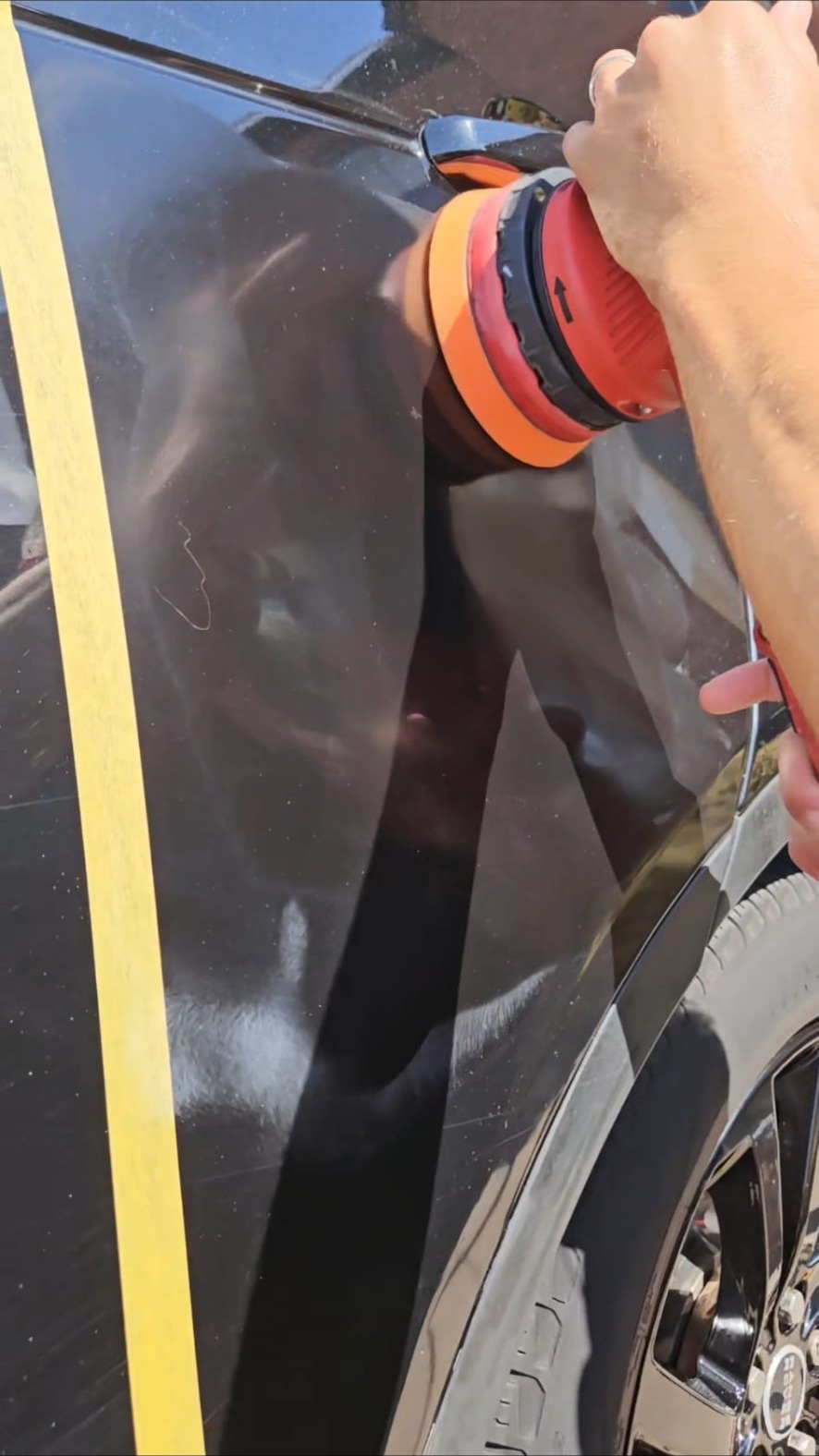 Machine polisher working beside masking tape on a dark wing