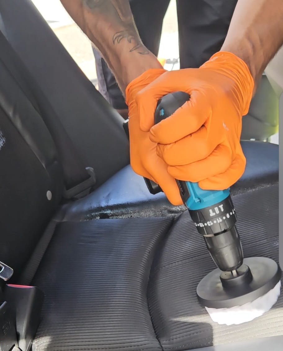 Fabric car seat being machine cleaned with a rotary brush and foam