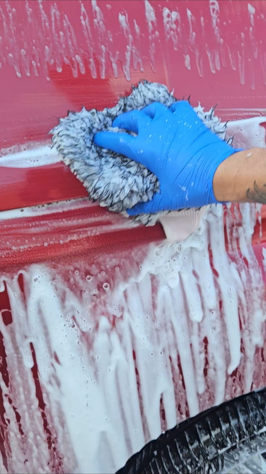 Blue-gloved hand washing red paint with a microfibre mitt