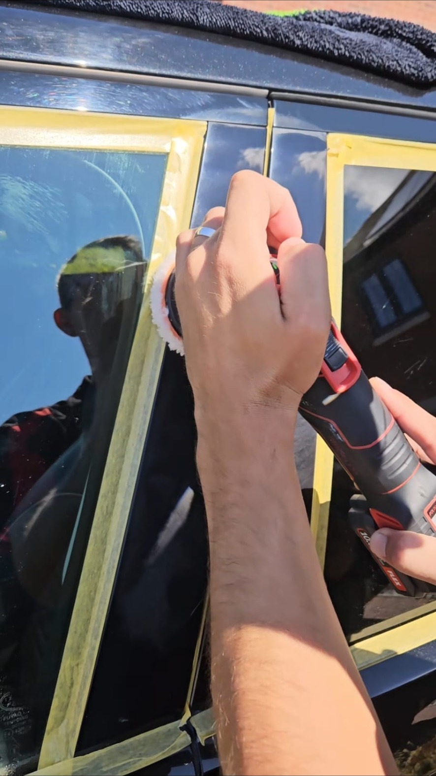 Small machine polisher refining a masked window pillar